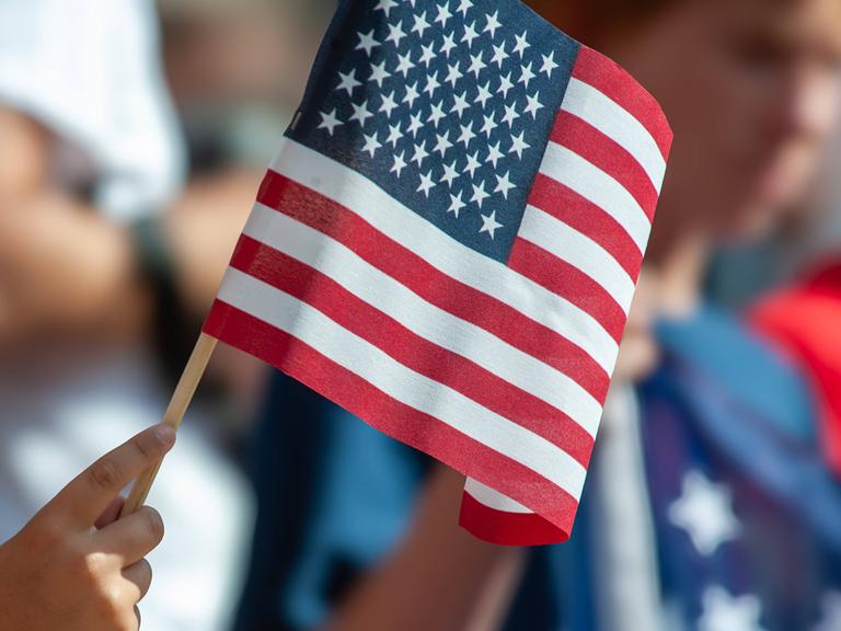 Nahaufnahme einer Hand, die eine amerikanische Flagge hält.