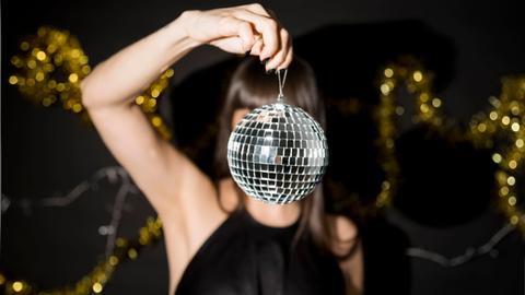 Eine junge Frau hält eine kleine Discokugel vor ihr Gesicht.