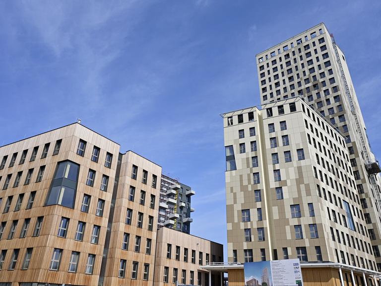 Ein Holz-Hybrid-Hochhaus ragt aus der Froschperspektive in den blauen Himmel.