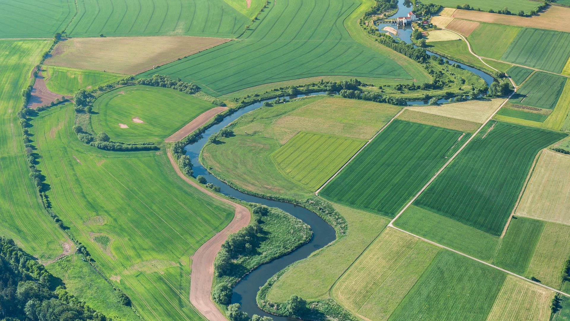 Luftaufnahme der Aue: Die Werra und das Grüne Band ziehen sich gewunden durch eine grüne Ackerlandschaft. Luftaufnahme der Aue: Die Werra und das Grüne Band ziehen sich gewunden durch eine grüne Ackerlandschaft.