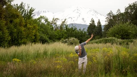 Teenager tanzt in ländlicher Umgebung vor Bergpanorama.