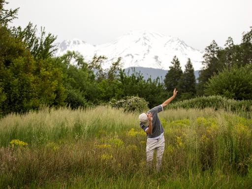 Teenager tanzt in ländlicher Umgebung vor Bergpanorama.