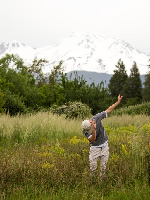 Teenager tanzt in ländlicher Umgebung vor Bergpanorama.
