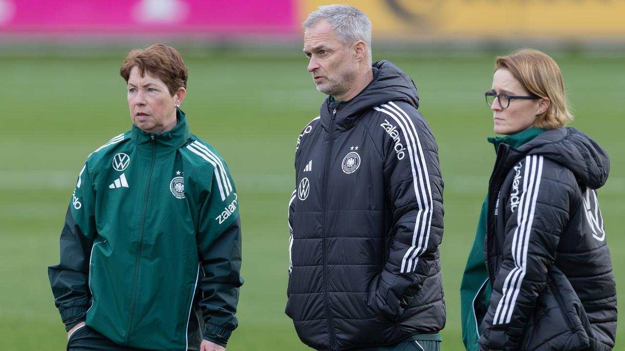 Bundestrainer Wück steht mit seinn Co-Trainerinnen Meinert (l. ) und Bartusiak (r.) auf einem Fußballplatz.