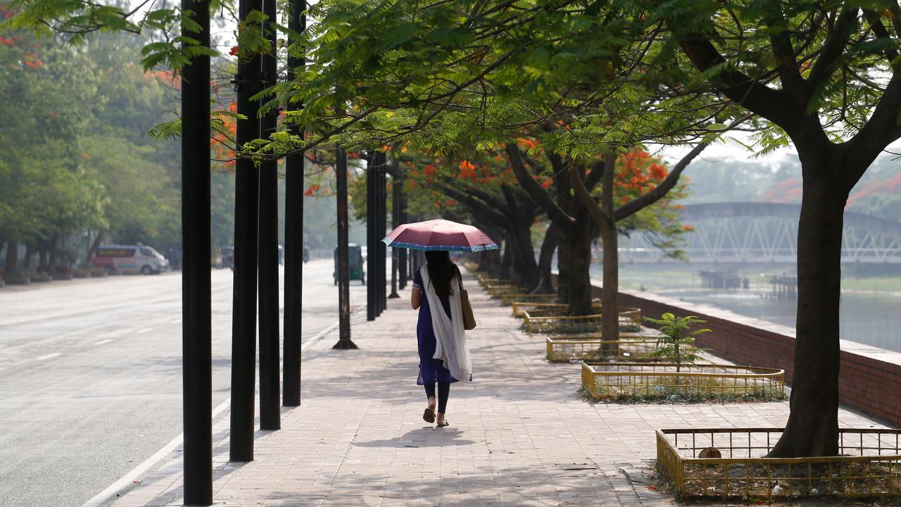 Ein Mädchen in Bangladesch läuft eine Straße entlang mit einem Schirm in der Hand, um sich vor der Sonne zu schützen. 