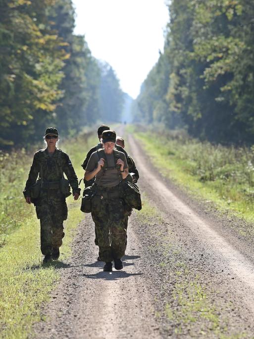 Drei uniformierte Frauen mit militärischer Ausrüstung auf einer Straße, die durch den Wald führt