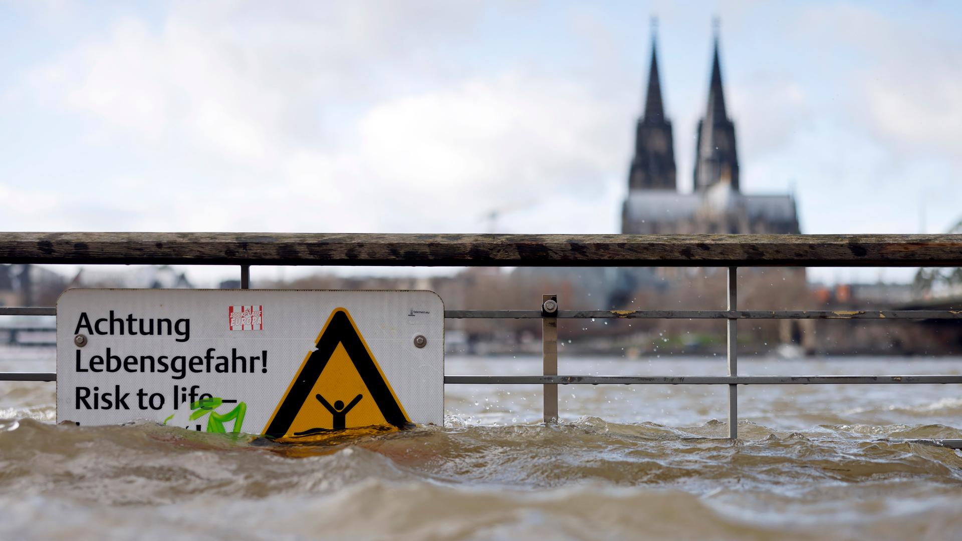 Am Ufer des überschwemmten Rhein in Köln. Ein Schild weist auf Lebensgefahr bei Hochwasser hin. 