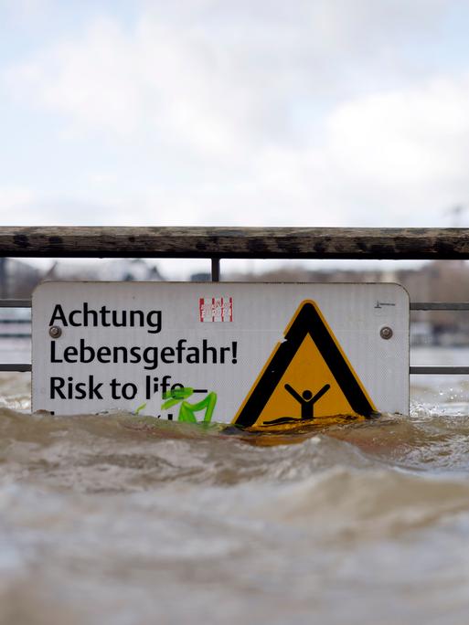 Am Ufer des überschwemmten Rhein in Köln. Ein Schild weist auf Lebensgefahr bei Hochwasser hin. 