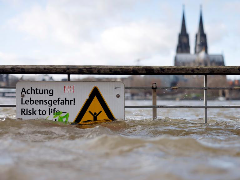 Am Ufer des überschwemmten Rhein in Köln. Ein Schild weist auf Lebensgefahr bei Hochwasser hin. 