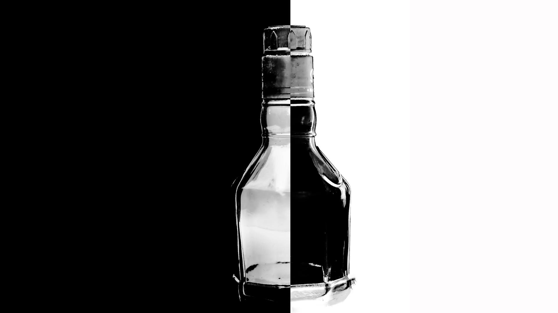 Nahaufnahme eines Glasflakons vor schwarz-weißem Hintergrund. Im Inneren der Flasche sind die Seiten vertauscht: schwarz auf weiß und weiß auf schwarz.