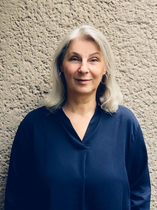 Ruth Olshan lächelt in die Kamera. Sie trägt eine blaue Bluse und kinnlanges graues Haar.