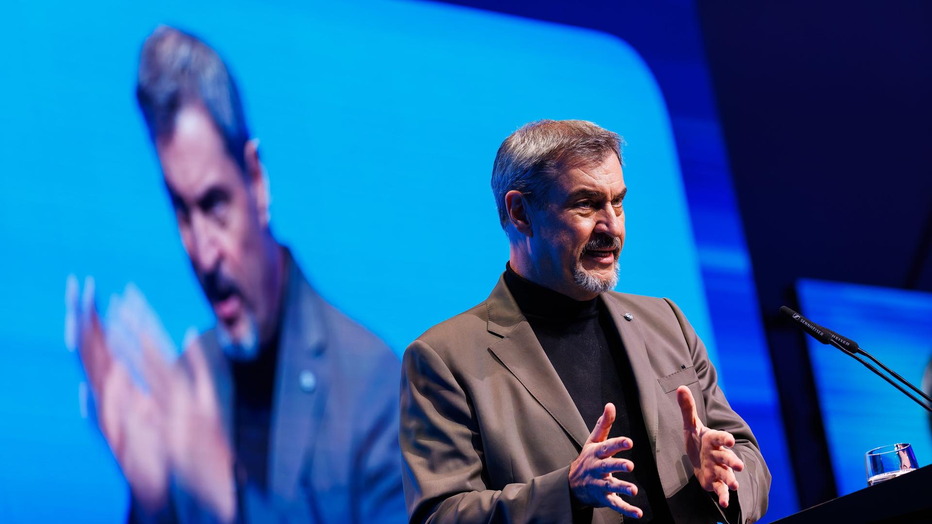 Man sieht Söder mit beiden Händen gestikulierend am Rednerpult. Hinter ihm sieht man ihn auf einer Videoleinwand gespiegelt.