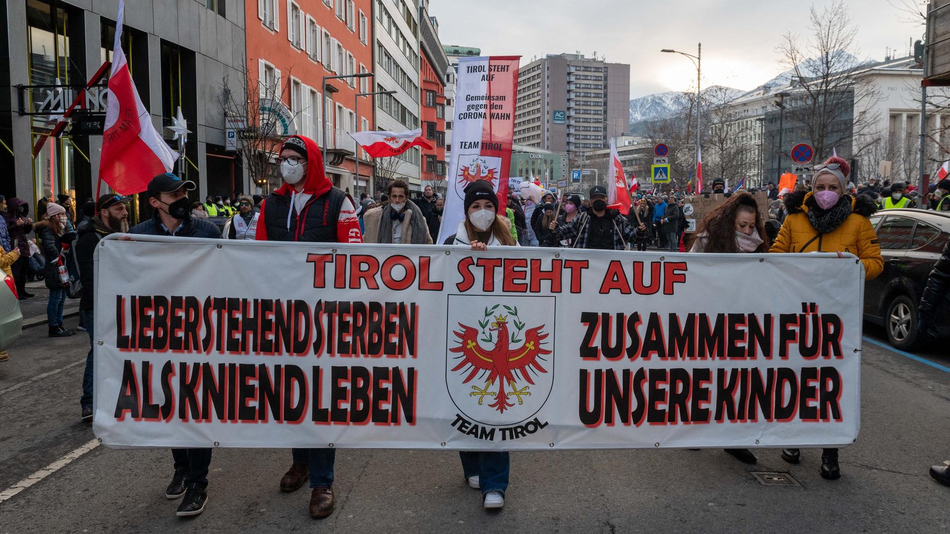 Proestierende tragen ein Banner mit der Aufschrift: "Tirol steht auf - Lieber aufrecht sterben als kniend leben. Zusammen für unsere Kinder". 