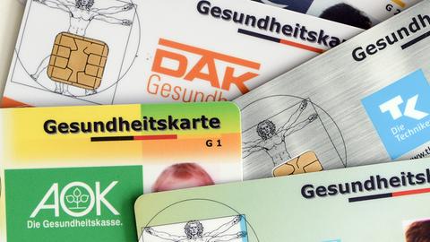 Mehrere Gesundheitskarten verschiedener Krankenkassen liegen auf einem Tisch.