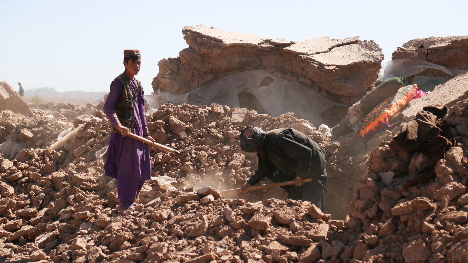 Zwei Männer in Afghanistan stehen mit Schaufeln auf einem Trümmerberg.