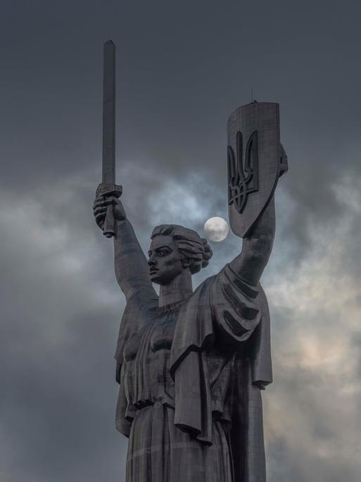 Motherland Monument, also called Mother Ukraine statue seen in Kyiv with clouds and the sun behind. The sculpture is part of the National Museum of the History of Ukraine in the Second World War and holds the Ukraine's coat of arms, the tryzub in its left hand. 