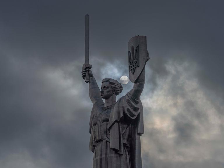 Motherland Monument, also called Mother Ukraine statue seen in Kyiv with clouds and the sun behind. The sculpture is part of the National Museum of the History of Ukraine in the Second World War and holds the Ukraine's coat of arms, the tryzub in its left hand. 