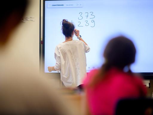 Ein Lehrerin schreibt eine Mathematikaufgabe auf eine digitale Schultafel im Klassenraum einer Schulklasse.