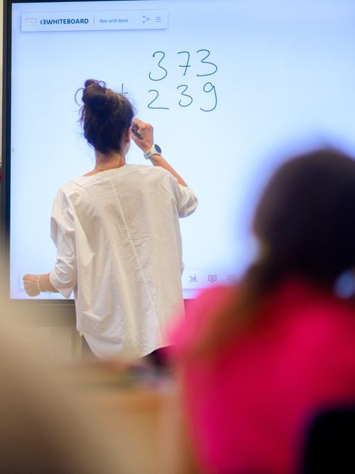 Ein Lehrerin schreibt eine Mathematikaufgabe auf eine digitale Schultafel im Klassenraum einer Schulklasse.