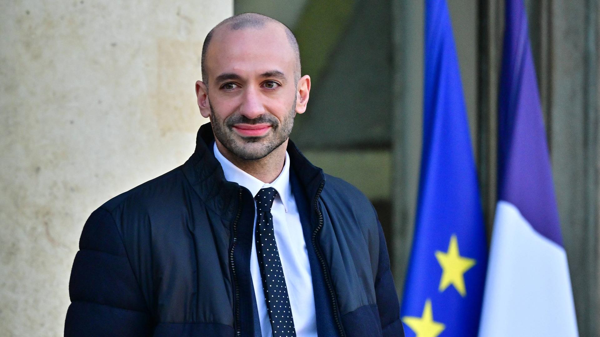 Benjamin Haddad steht vor dem Elysee-Palast, links hinter ihm die französische und die EU-Fahne.