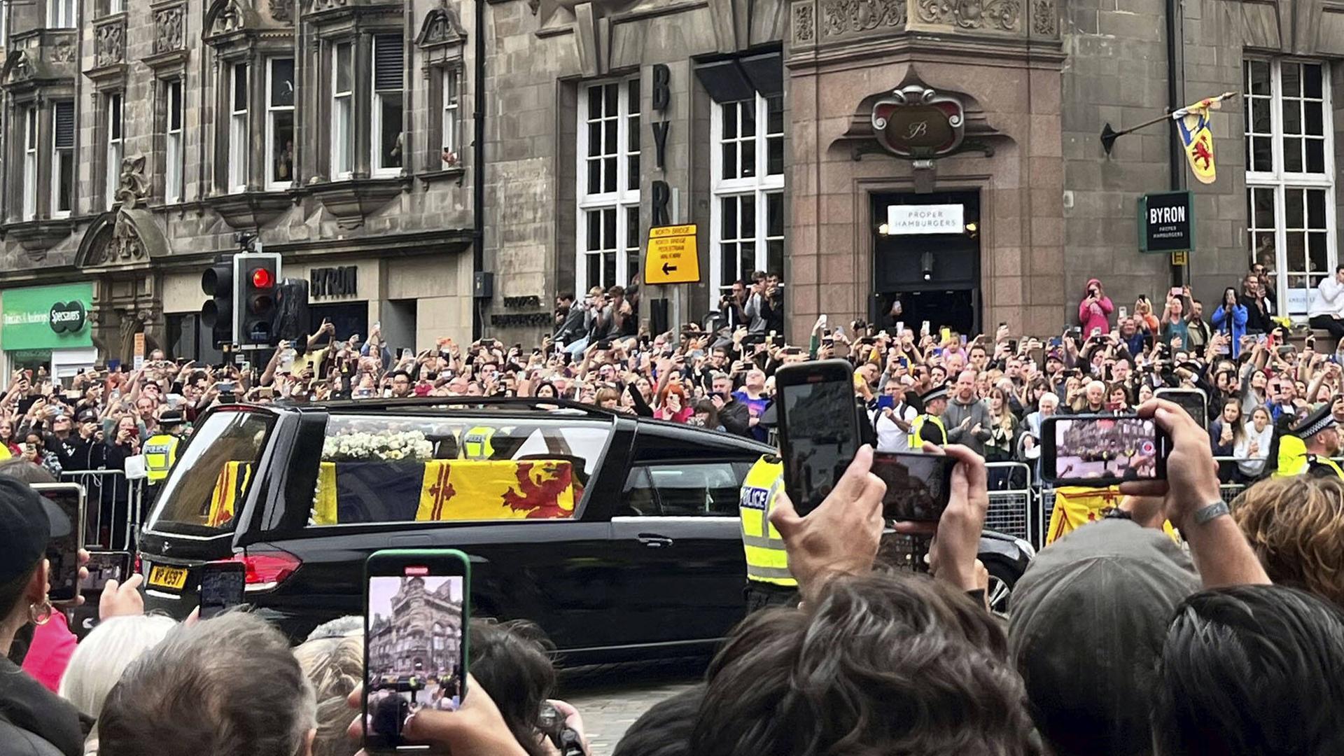 Menschenmengen versammeln sich auf einer Straße in Edinburgh, um den Leichenwagen zu beobachten, der den Sarg von Königin Elizabeth II. transportiert. Menschenmengen versammeln sich auf einer Straße in Edinburgh, um den Leichenwagen zu beobachten, der den Sarg von Königin Elizabeth II. transportiert.