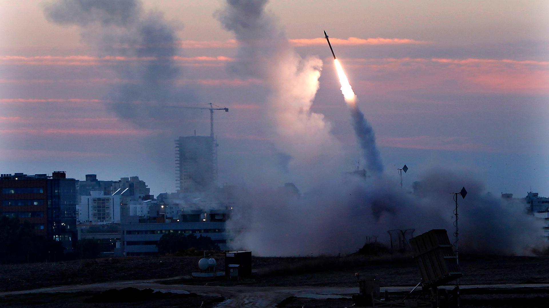Das Bild zeigt das Iron Dome Abwehrsystem in Israel. Rauchwolken und eine Rakete vor einem rot gefärbten Himmel.