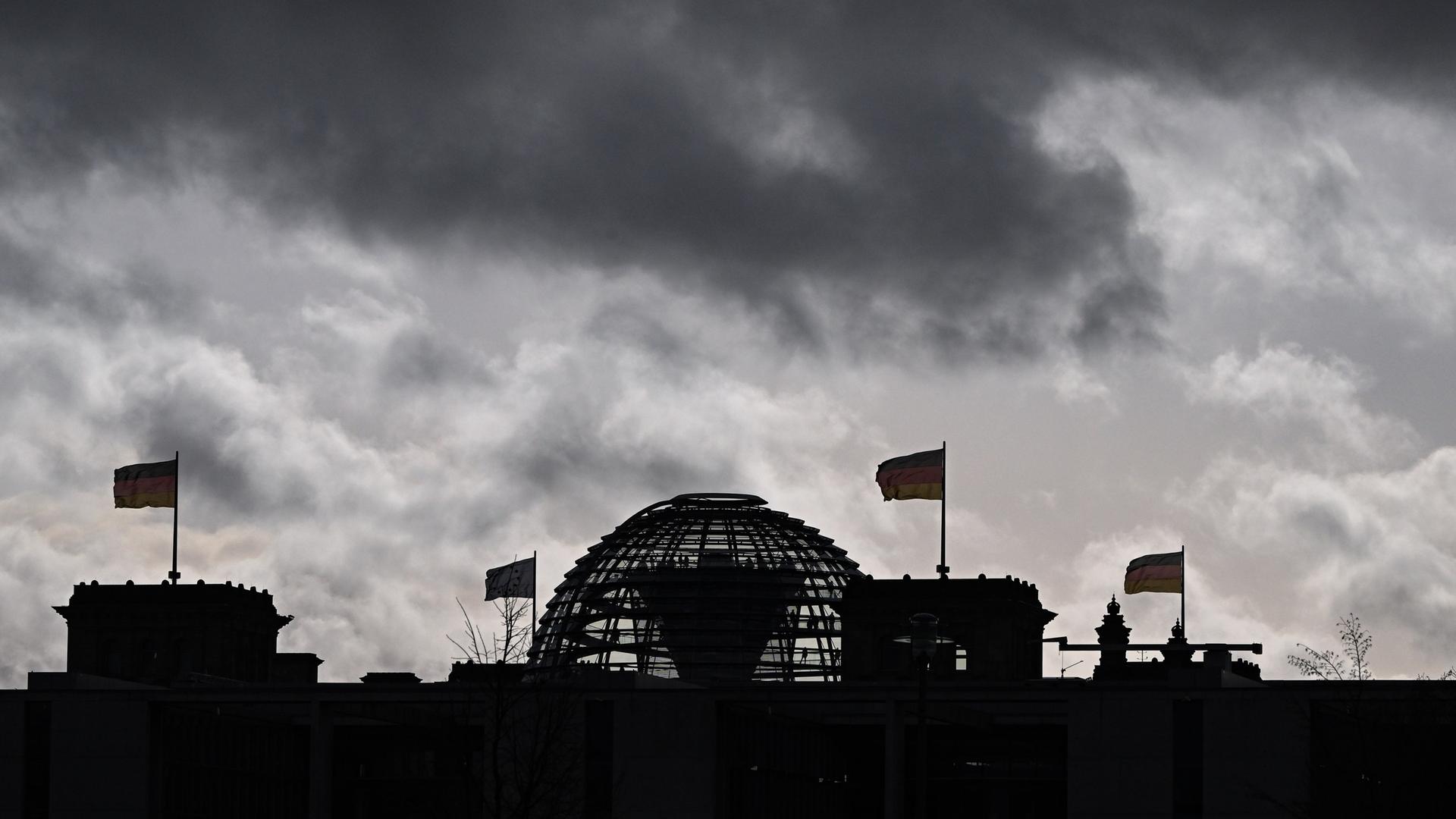 Wolken sind über der Kuppel vom Reichstag zu sehen, auf dem Deutschlandfahnen wehen.