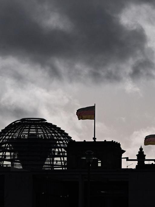 Wolken sind über der Kuppel vom Reichstag zu sehen, auf dem Deutschlandfahnen wehen.