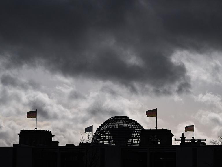 Wolken sind über der Kuppel vom Reichstag zu sehen, auf dem Deutschlandfahnen wehen.