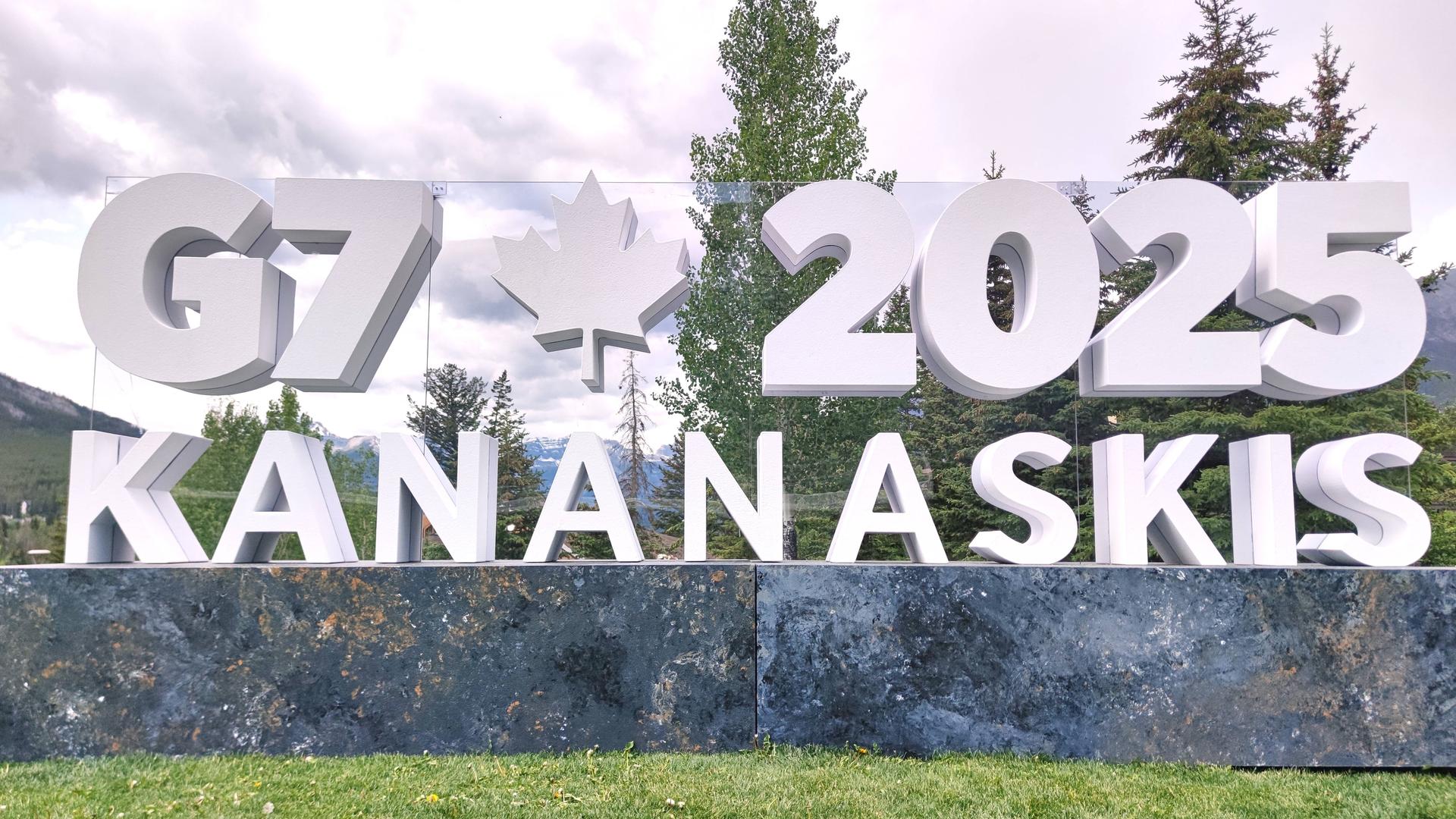 In einer Landschaft mit Wald stehen weiße Buchstaben. Die bilden das Logo für den G7-Gipfel in Kanada. 