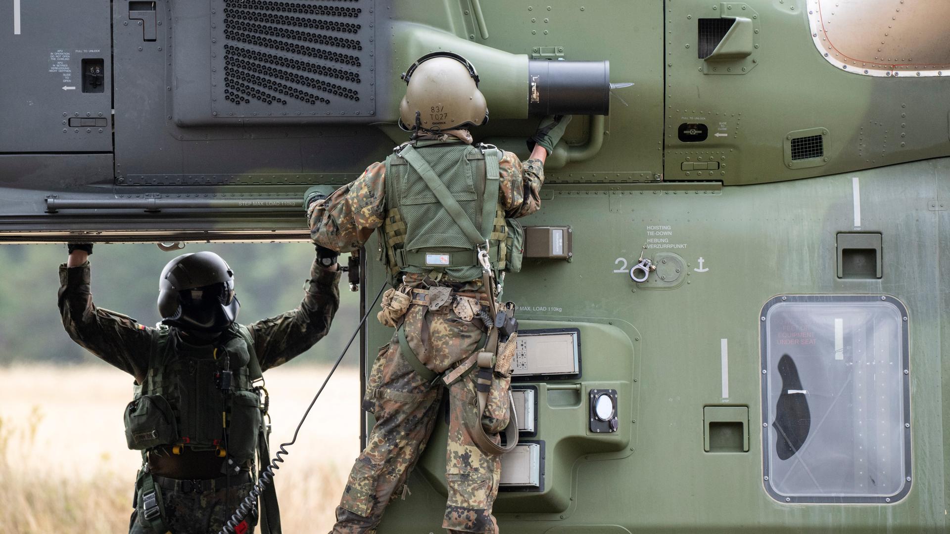 Besatzungsmitglieder prüfen einen NH90 Helikopter auf einem Feld. 