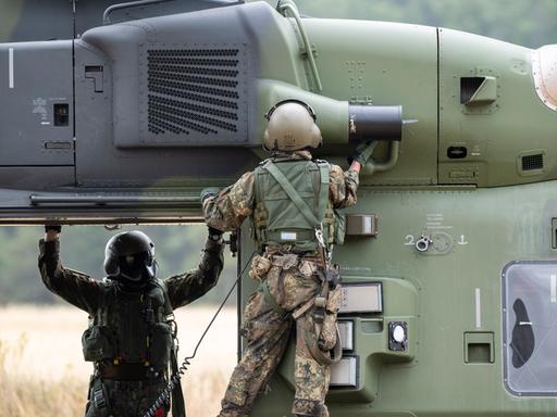 Besatzungsmitglieder prüfen einen NH90 Helikopter auf einem Feld. Besatzungsmitglieder prüfen einen NH90 Helikopter auf einem Feld.