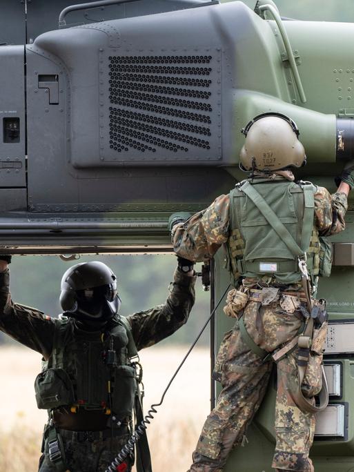 Besatzungsmitglieder prüfen einen NH90 Helikopter auf einem Feld. Besatzungsmitglieder prüfen einen NH90 Helikopter auf einem Feld.