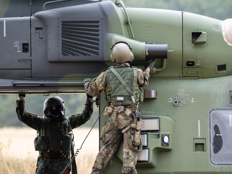 Besatzungsmitglieder prüfen einen NH90 Helikopter auf einem Feld. Besatzungsmitglieder prüfen einen NH90 Helikopter auf einem Feld.