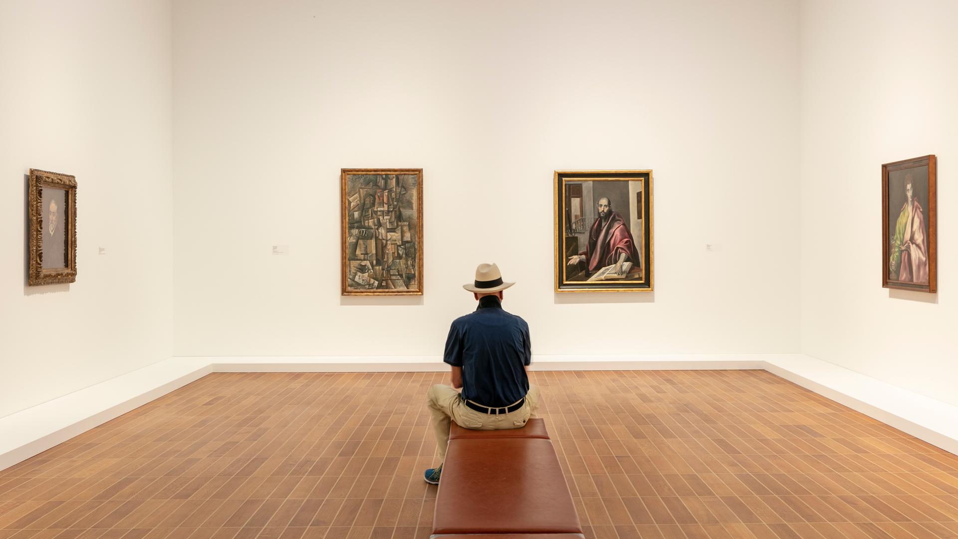 Ausstellungsansicht: Ein Mann sitzt auf einer Bank und betrachtet die Werke von Picasso und El Greco.