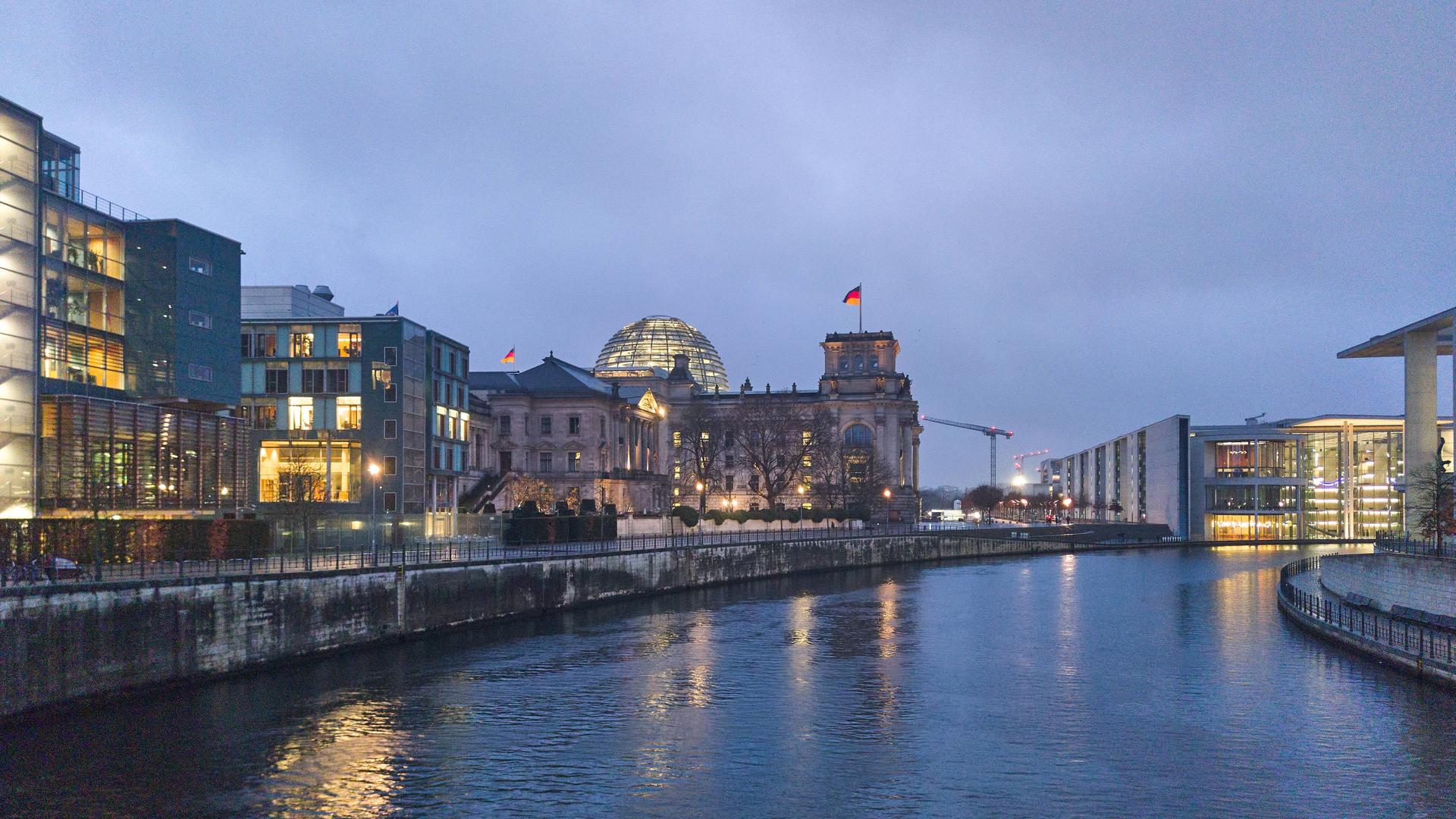 Das Reichstagsgebäude in Berlin bei Nacht, das Gebäude ist beleuchtet, rechts davon verläuft die Spree.