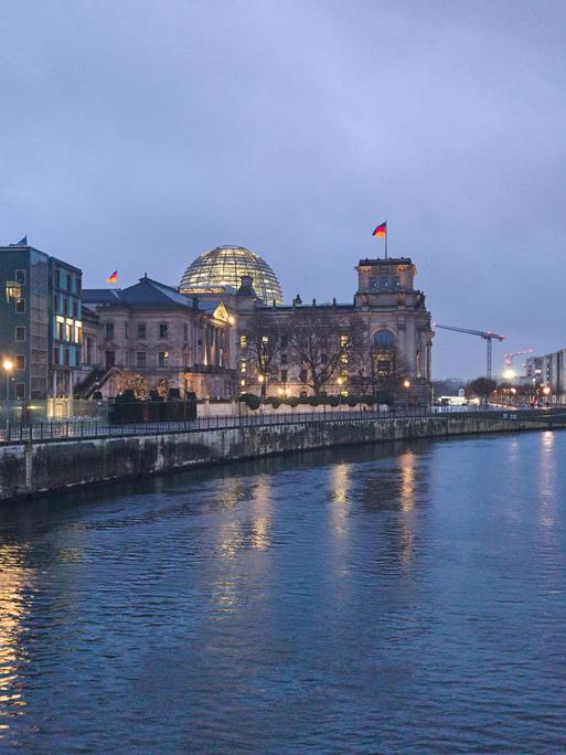 Das Reichstagsgebäude in Berlin bei Nacht, das Gebäude ist beleuchtet, rechts davon verläuft die Spree.