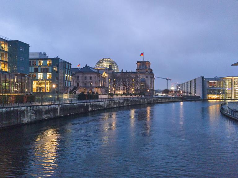 Das Reichstagsgebäude in Berlin bei Nacht, das Gebäude ist beleuchtet, rechts davon verläuft die Spree.