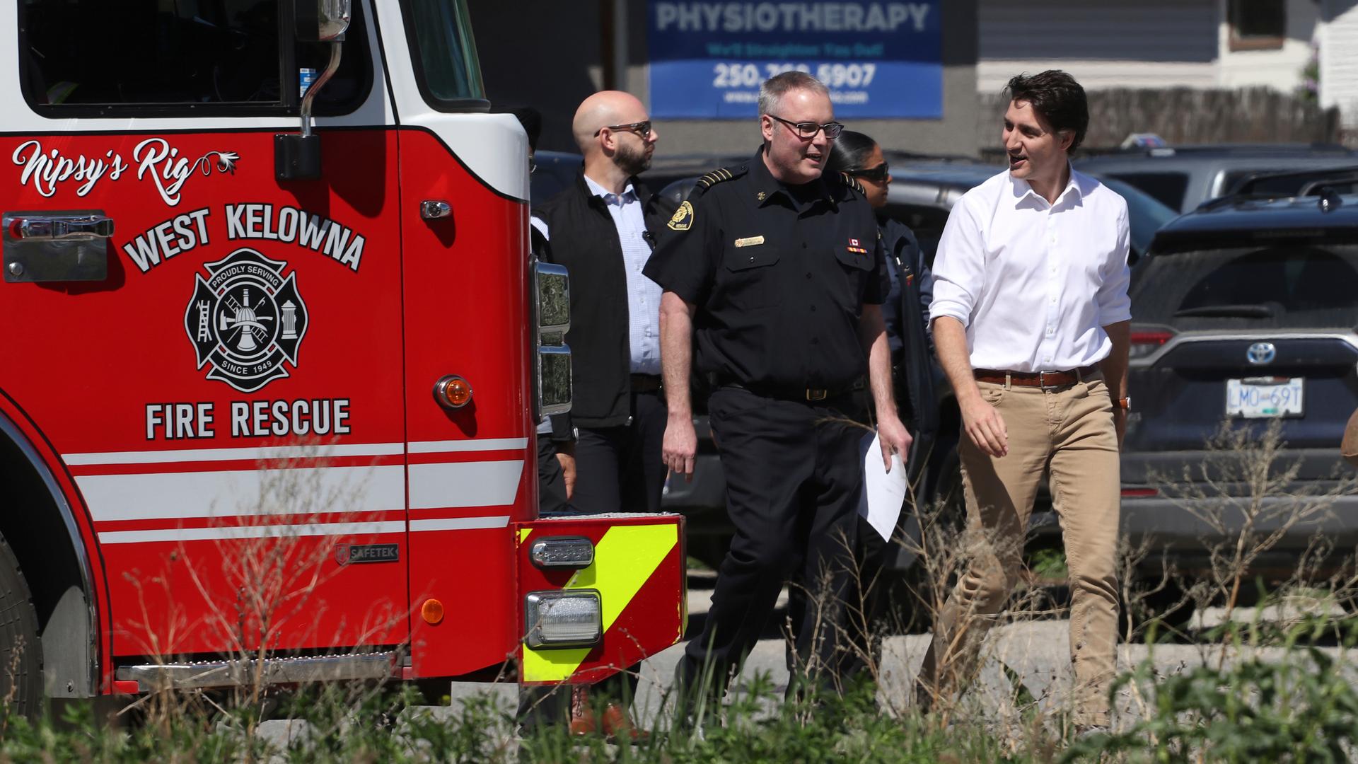 Kanadas Premierminister Trudeau steht in den Waldbrandgebieten von British Columbia gemeinsam mit Einsatzkräften neben einem Feuerwehrfahrzeug. 