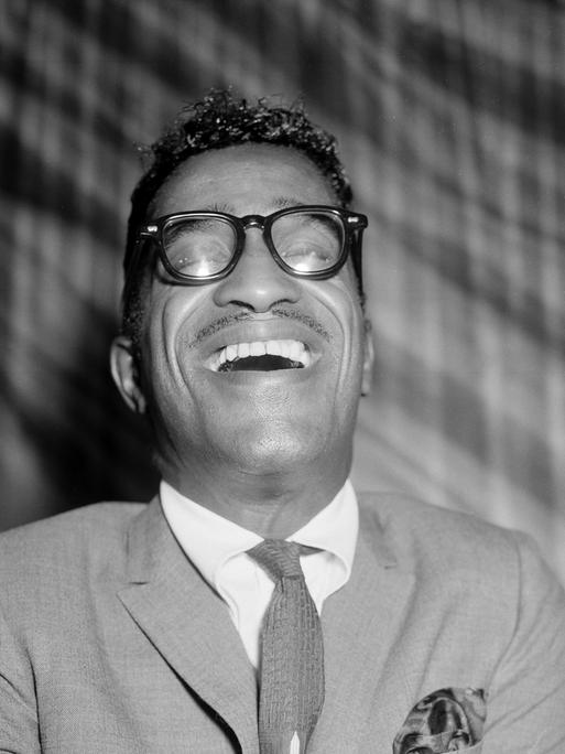 Schwarzweißporträt von Sammy Davis Jr. lachend in einem Londoner Restaurant 1960.