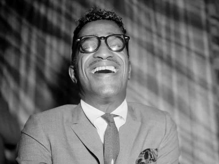Schwarzweißporträt von Sammy Davis Jr. lachend in einem Londoner Restaurant 1960.