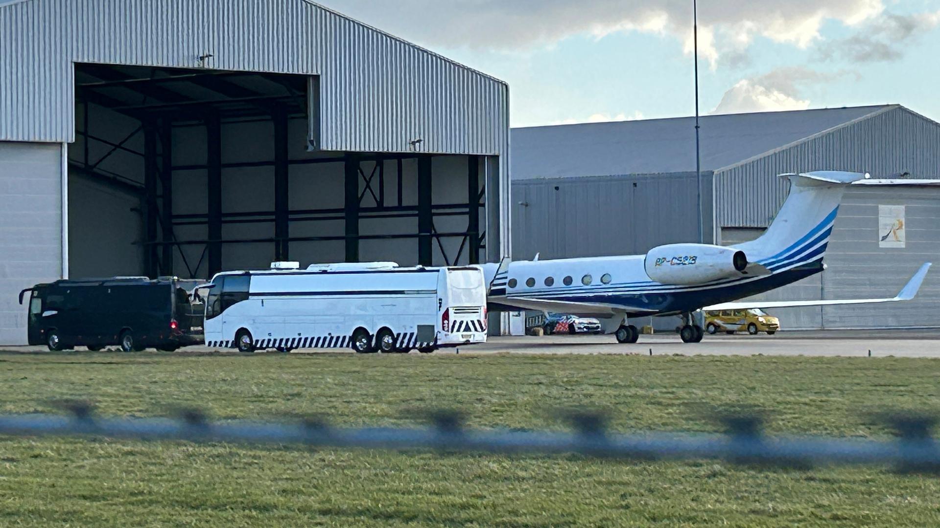 Ein Flugzeug steht vor einem Hangar am Flughafen Rotterdam, daneben ein Gefängnisbus.