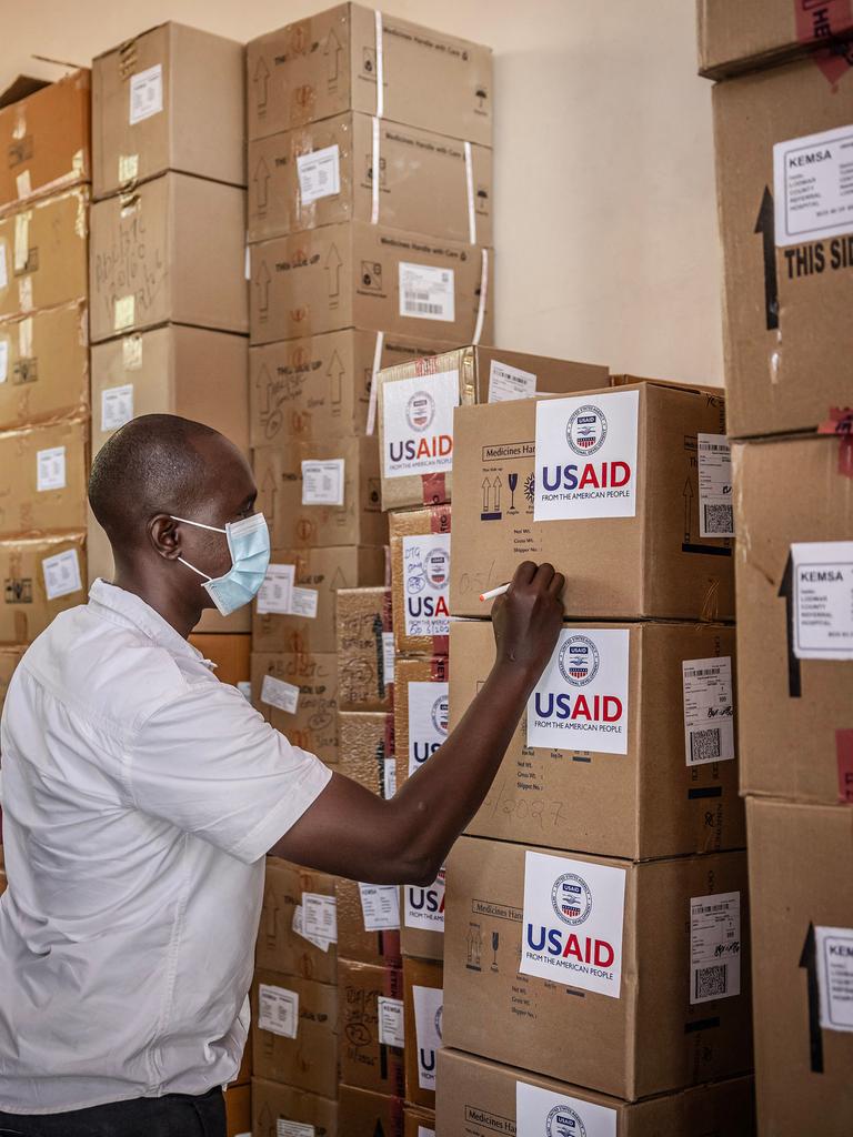 Zwei Personen beschriften in einem Lager aufeinandergestapelte Kartons mit der Aufschrift "USAID".