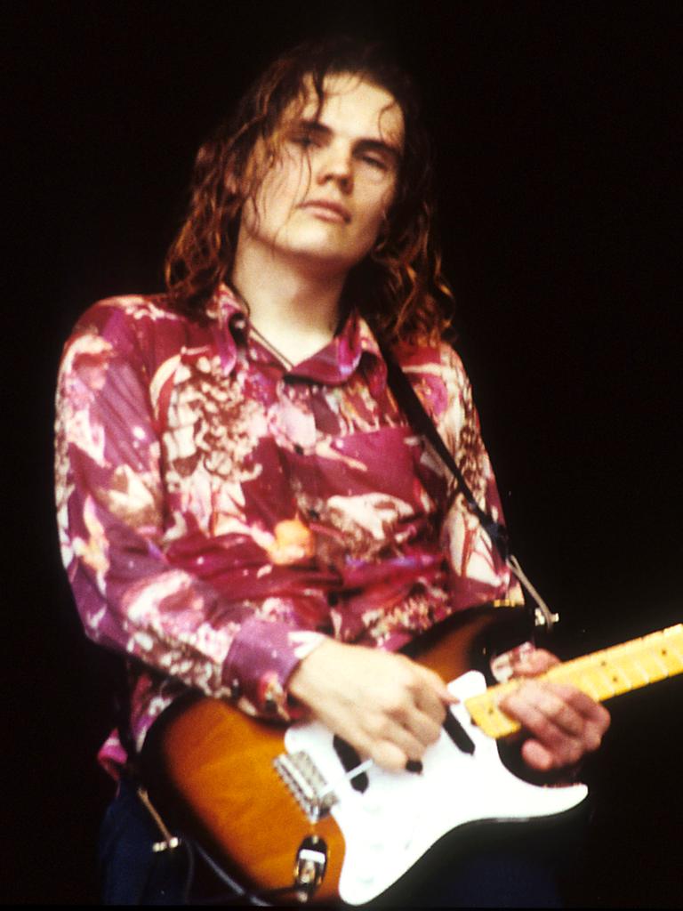 Billy Corgan von Smashing Pumpkins steht in den 90er-Jahren mit seiner Gitarre, rot geblümten Hemd und offenem Haaren auf einer Bühne.