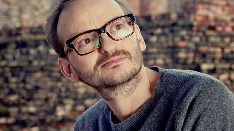 Milan Peschel steht vor einer Backsteinmauer und schaut nach rechts oben. Milan Peschel steht vor einer Backsteinmauer und schaut nach rechts oben.