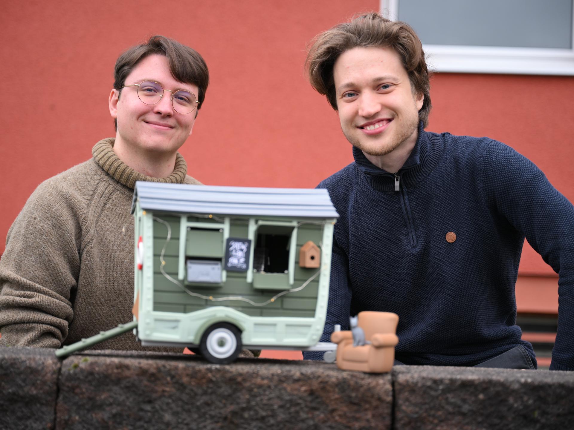 David Zapfe-Wildemann und Raven Rusch von dem Kölner Independent-Gamingstudio Neoludic stehen vor einem Haus, in dem ihre Firma ihren Sitz hat. Vor sich halten sie das Model eines Wohnwagen in Form eines Hauses. David Zapfe-Wildemann und Raven Rusch von dem Kölner Independent-Gamingstudio Neoludic stehen vor einem Haus, in dem ihre Firma ihren Sitz hat. Vor sich halten sie das Model eines Wohnwagen in Form eines Hauses.