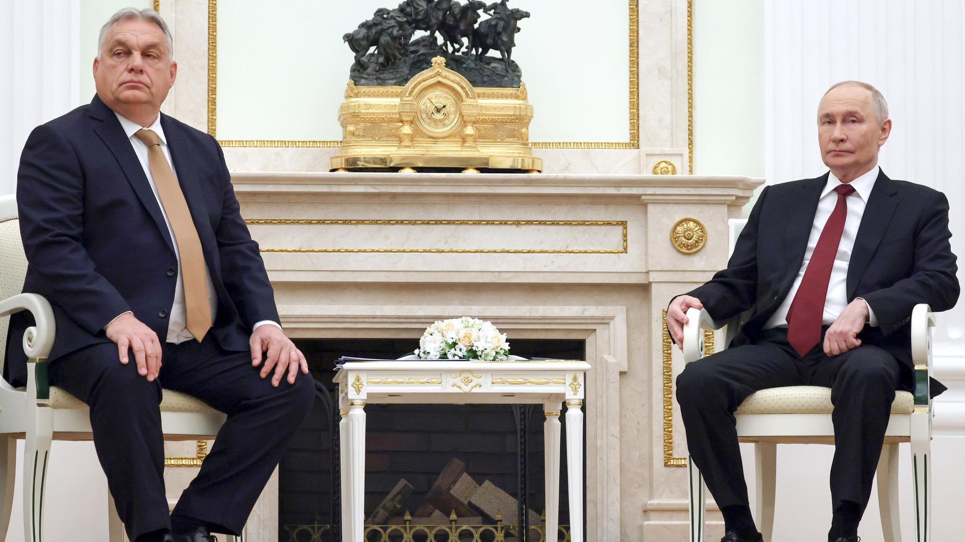 Orban und Puten sitzen nebeneinander auf Stühlen, zwischen ihnen steht ein kleiner Tisch.