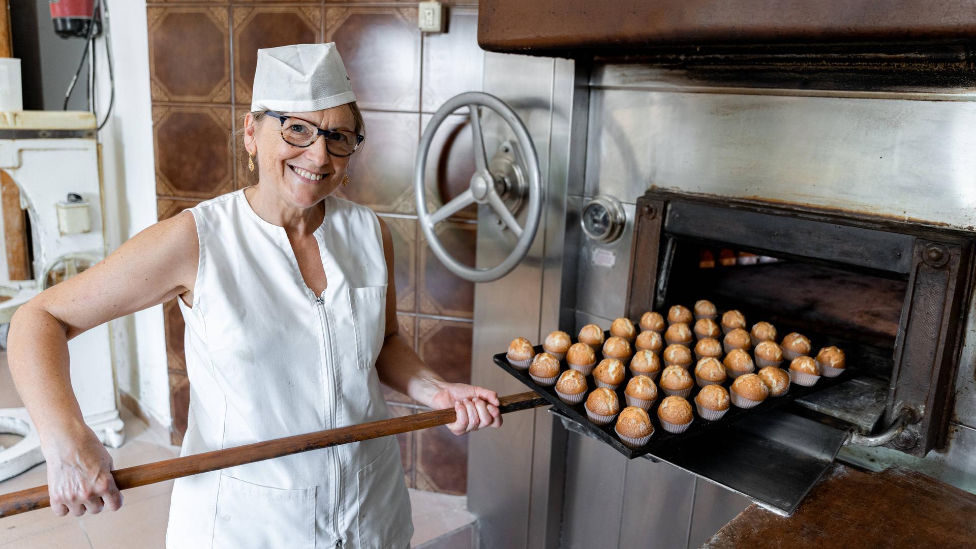 Bäckerin mit weißer Mütze holt frischgebackene Muffins aus dem Ofen Bäckerin mit weißer Mütze holt frischgebackene Muffins aus dem Ofen