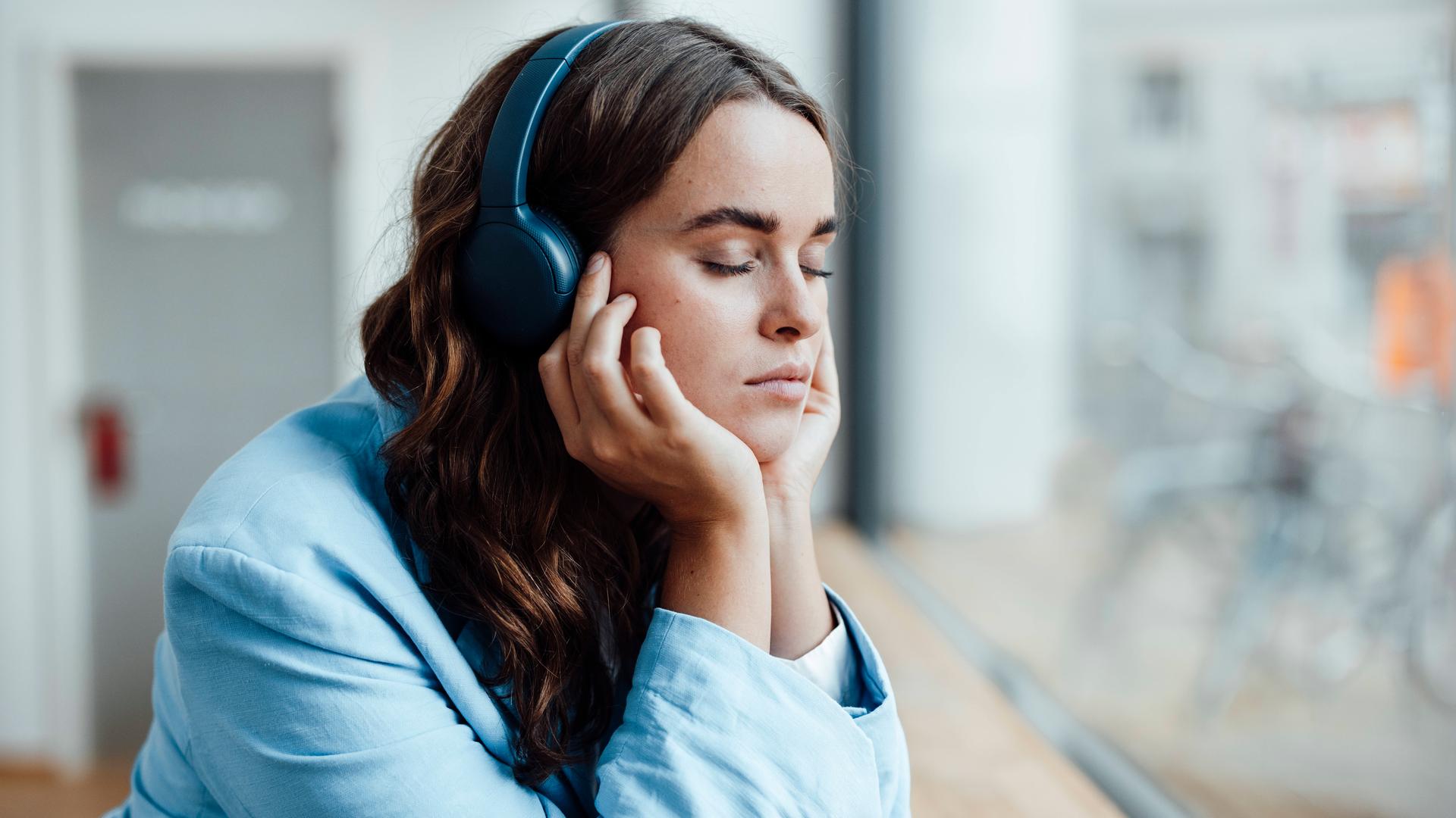 Businesswoman with eyes closed listening music through wireless headphones in office model released property released, G