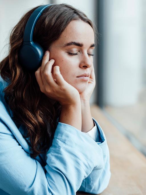 Businesswoman with eyes closed listening music through wireless headphones in office model released property released, G